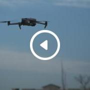 A drone in the sky, mid-flight, with an overlay image of a play button. 